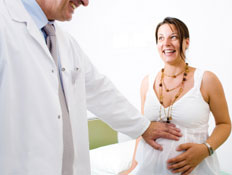 רופא מחייך בחלוק לבן בודק בטן של אישה בהריון צוחקת (צילום: nyul, Istock)